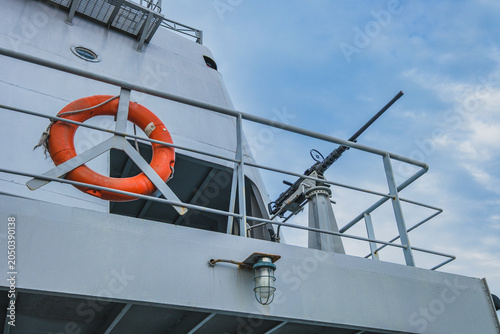 Картината върху платно Low angle view of a naval ship deck with an orange lifebuoy and machine gun