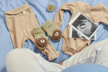 Pregnant woman looking at baby clothes and ultrasound scan photos