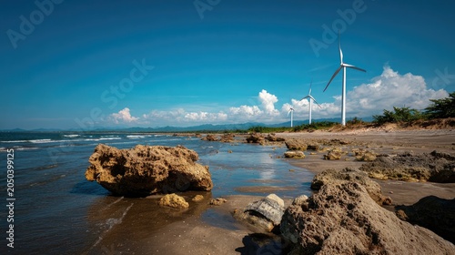 Coastal scene with rocky shoreline, ocean, and renewable energy wind turbines under blue sky