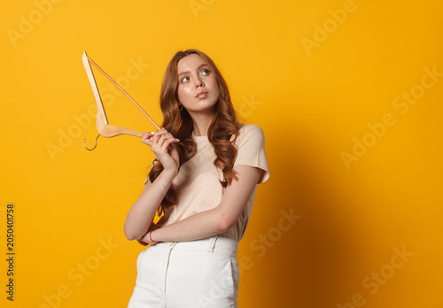 Young woman holding an empty clothes hanger on a yellow background. Fashion retail, wardrobe planning and shopping concept.