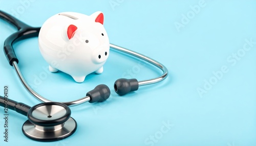 White ceramic piggy bank and stethoscope on light blue background
