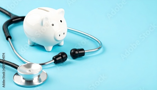 White ceramic piggy bank and stethoscope on light blue background