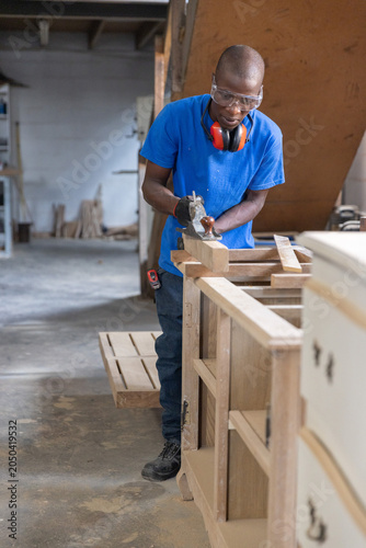 Hand plane smoothing unfinished wooden panel on workbench with scattered sawdust and cabinet frames