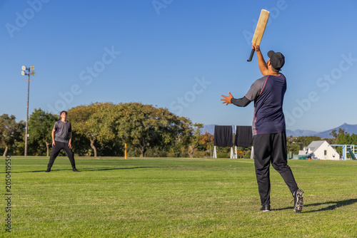 Φωτογραφία Male teammates batting and teenage fielder practicing on field with wooden crick