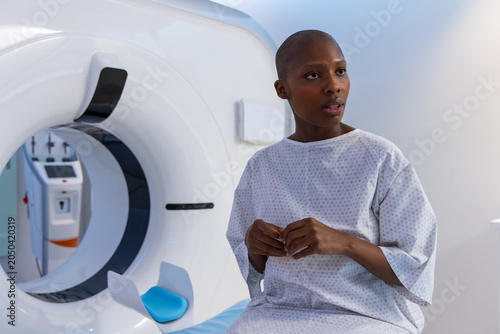African female patient sitting on scan table beside imaging gantry with blue headrest, copy space