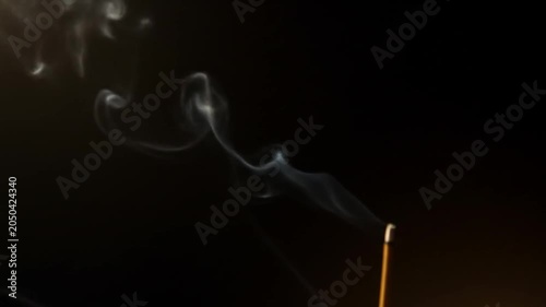 Wisps of incense smoke curl upwards against a dark background.