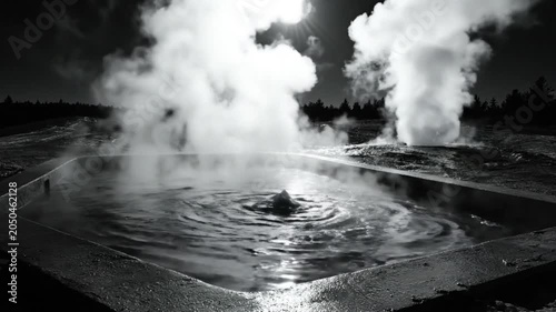 Black and white view of a steaming hot spring with swirling water and plumes of vapor in natural landscape