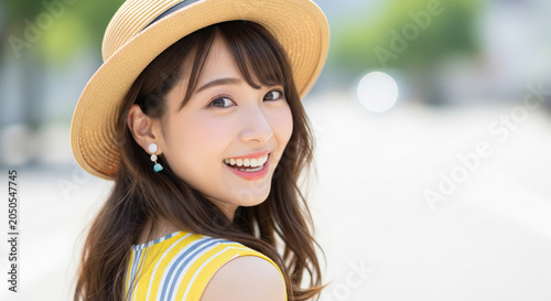 街角で麦わら帽子を被り振り返りながら微笑むストライプ柄トップスの女性