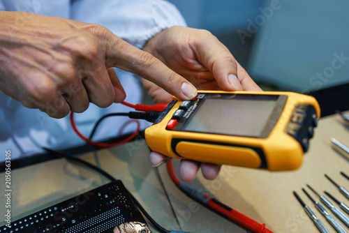 Konstfotografi Close-up of a technician using a handheld digital tester with probe wires at a workbench, checking electronic equipment during repair or maintenance