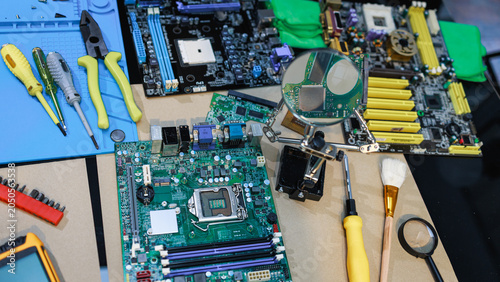 Photos Computer repair workspace with motherboards, hard drive parts, screwdrivers, pliers and magnifier on a table, showing electronics maintenance, upgrade, recycling and technical service
