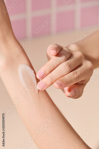 Quadro su tela Close-up of hand talent applying white skincare cream on forearm against pink mosaic tile background