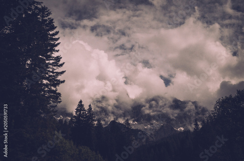 Fotografie Dark clouds and forest silhouettes create a dramatic and mysterious view of the Dachstein Mountains