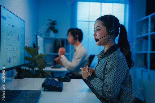 Gen z Asia young call center team or customer support service executive use computer and microphone headset work technical e commerce support in late night office. Telemarketing or sales job concept.