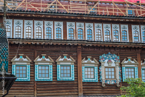 Traditional Russian wooden building showcases intricate window designs and colorful decorations, with scaffolding indicating ongoing renovation work