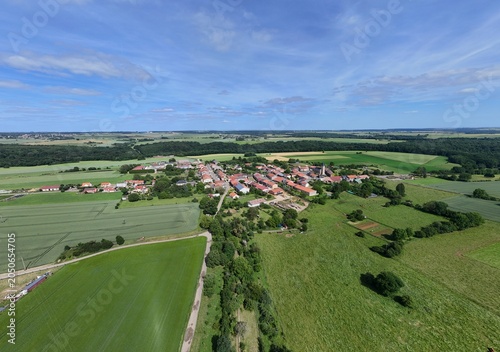 Vue aérienne panoramique du village de Laix, en Meurthe-et-Moselle, Lorraine. La commune rurale avec ses habitations et ses bâtiments entourée de champs et de cultures. Ciel bleu et nuages