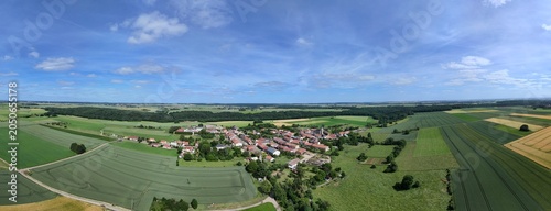 Vue aérienne panoramique du village de Laix, en Meurthe-et-Moselle, Lorraine. La commune rurale avec ses habitations et ses bâtiments entourée de champs et de cultures. Ciel bleu et nuages