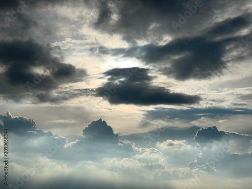 Dark thunderstorm clouds over bright white cumulus clouds with sunlight.