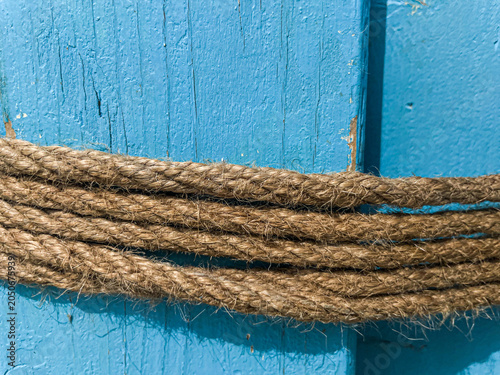 Landscape close up full frame view of thick twisted brown jute rope wrapped horizontally across a bright blue painted wooden surface
