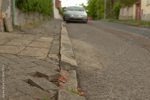 Принти на полотні Close low-angle view of a deteriorated concrete curb and uneven paved sidewalk next to an asphalt residential road