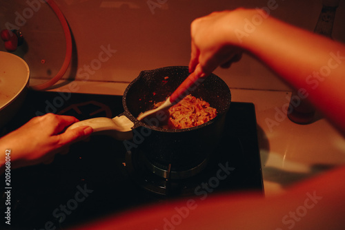 Person Cooking Food in Pan on Stove with Spoon.