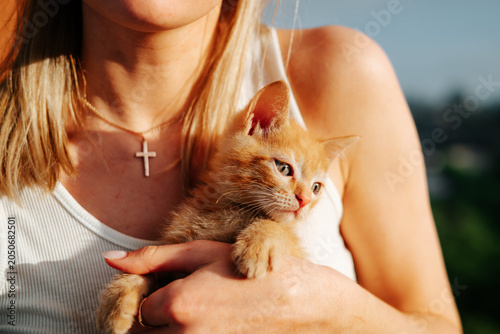 Принти на полотні A woman gently cradles a small orange kitten in her arms while standing outdoors