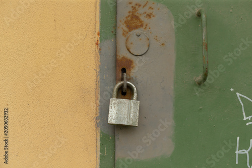 Foto Close-up view of an aged silver padlock hanging from a hasp on a green metal door next to a beige painted wall