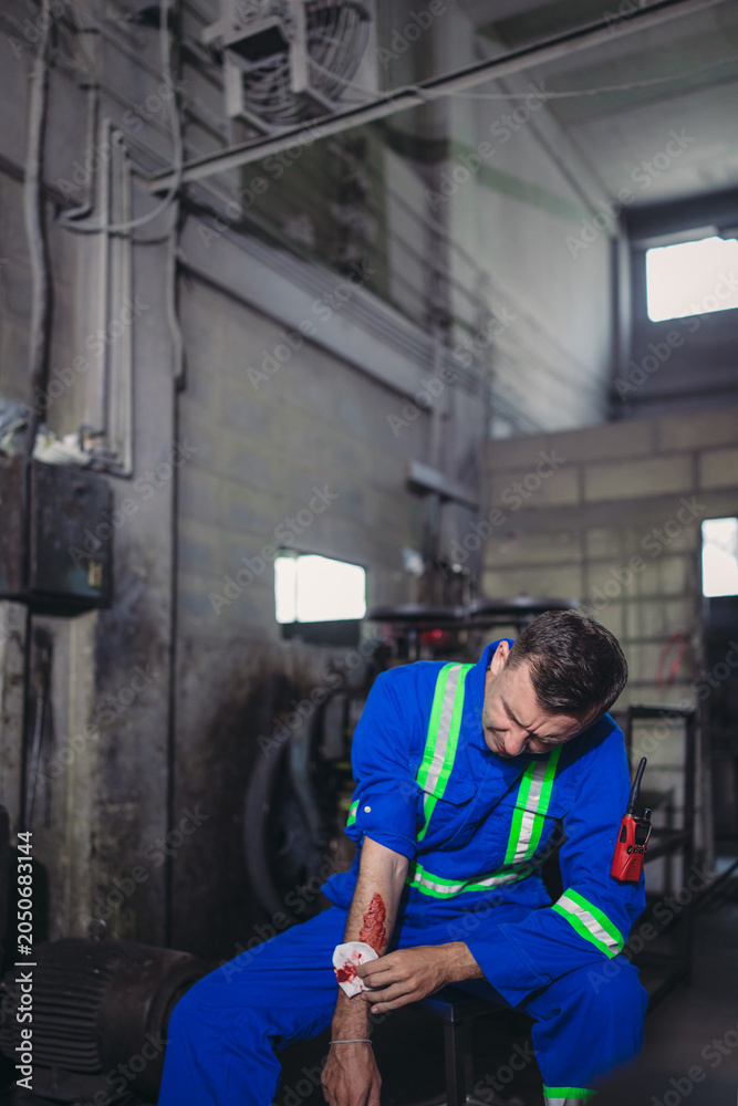 Obraz premium Industrial worker bandaging injured hand after workplace accident in factory maintenance shop