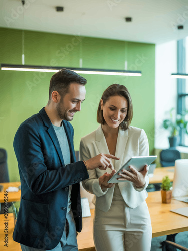 Businessman and Businesswoman Discussing on Tablet in Modern Office