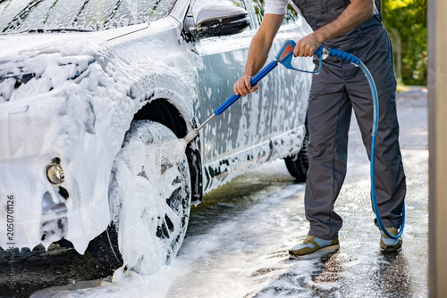 Fotografie A person in overalls uses a pressure washer to clean the wheels and body of a ca