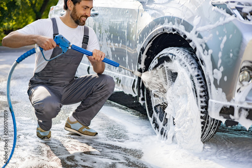 Quadro su tela A man in overalls is pressure washing a car wheel with a hose and foam