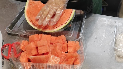 A shop assistant at the fruit store is slicing watermelon