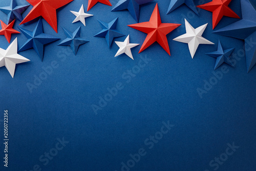 Festive arrangement of red, white and blue paper stars and curled ribbons on dark blue background. Patriotic border with empty space for text, suitable for Independence, Fourth of July, Memorial