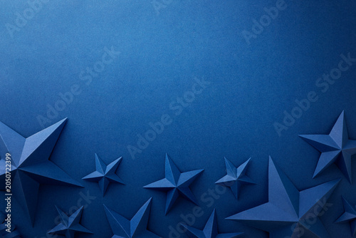 Monochrome blue composition with folded paper stars arranged around the edges on a dark blue background. Patriotic border with empty space for text, suitable for Independence, Fourth of July, Memorial
