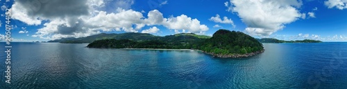 Panoramic drone view of Mahé's lush coastline from Anse Louis to Anse La Mouche, Seychelles, featuring vibrant tropical mountains, blue Indian Ocean waters, and dramatic skies