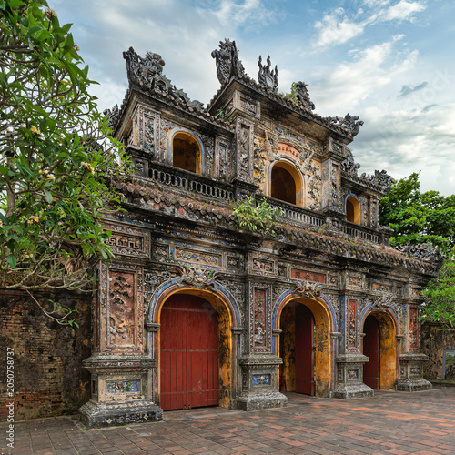 Ornate Hien Nhon Gate, Imperial City, Hue, Vietnam. Ancient traditional architecture with intricate details, weathered facade, and lush trees under a cloudy sky