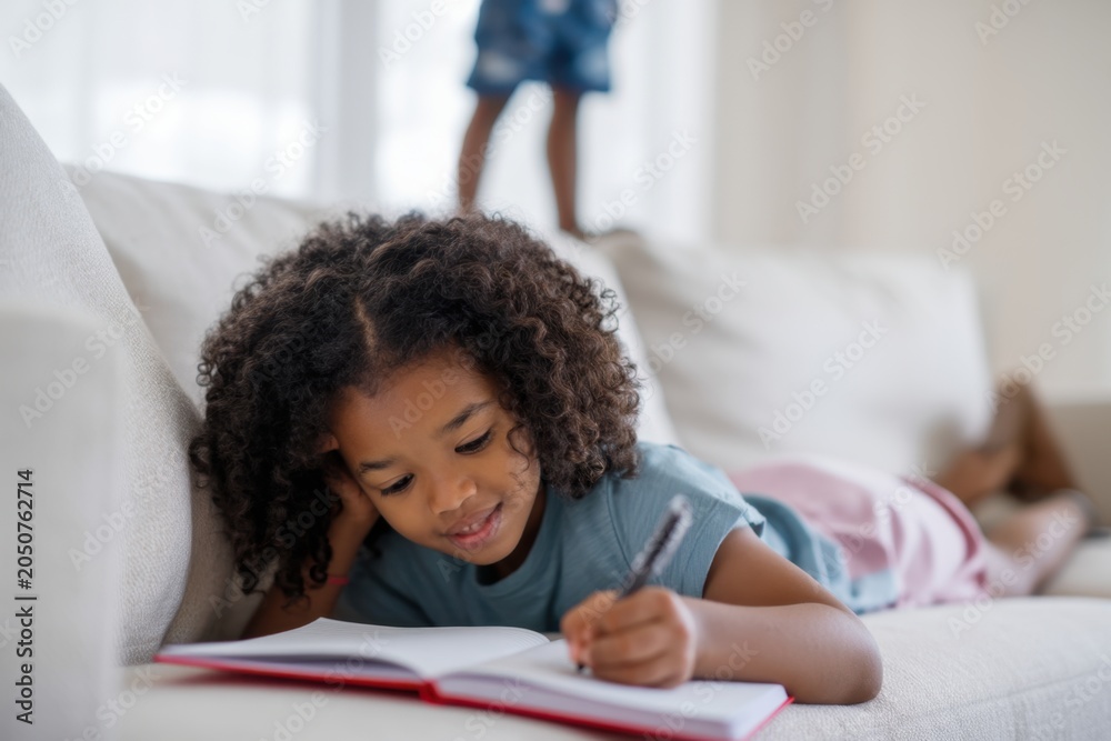 Fototapeta premium The girl writing in a notebook on a living room sofa during study