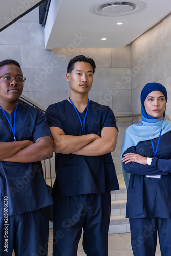 Diverse healthcare team posing with arms crossed in hospital wearing navy scrubs and blue lanyards