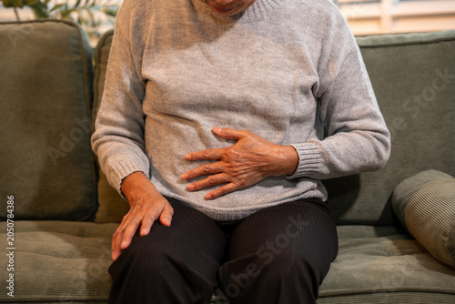 Schilderij op canvas Senior woman sitting on a sofa and holding her stomach, showing abdominal pain,