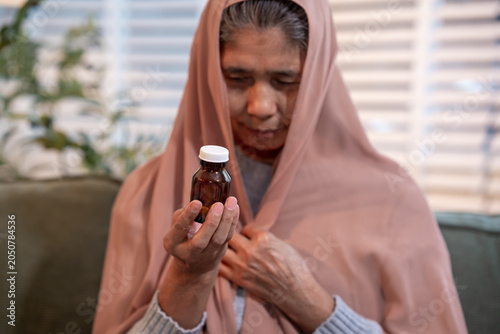 Foto Senior woman wrapped in a shawl sitting on a sofa at home and checking a medicin