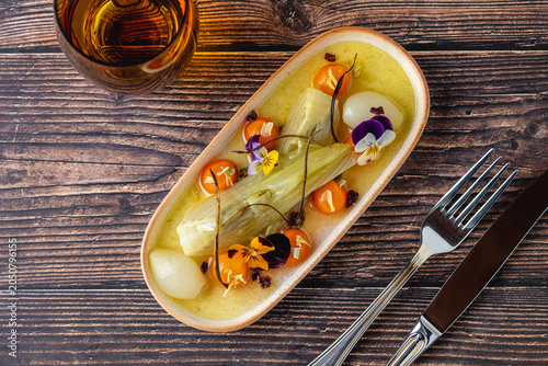 Gourmet braised leek dish served with pearl onions and edible flowers