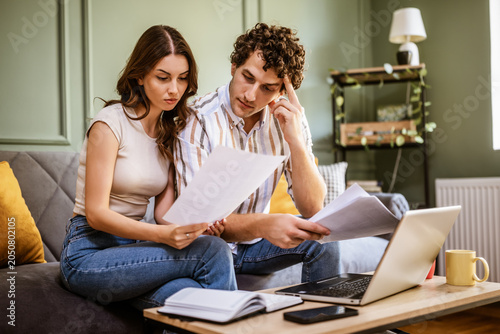 A couple carefully examines documents while using a laptop at home. The image highlights teamwork, communication, and the importance of staying organized when managing personal finances.
