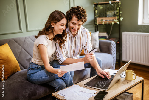 A woman holds a bill or statement while speaking with her partner on the sofa. Their are working together to understand expenses, manage finances, or plan upcoming payments.