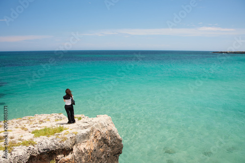 A woman standing at the edge of a cliff overlooking the sea in Monopoli, Puglia, Italy