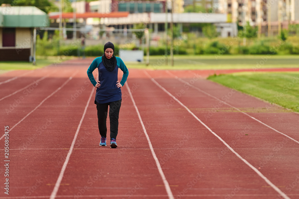 Fototapeta premium Muslim Woman in Hijab Walking on Outdoor Running Track During Solo Fitness Training