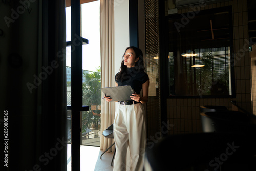 Asian businesswoman looking out window holding tablet thinking