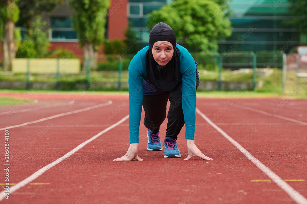 Obraz premium Female Hijab Runner On Track Starting Sprint Pose Showing Determination Fitness And Athletic Focus