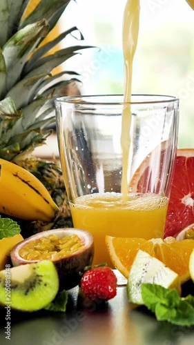 fruit juice pouring into glass with tropical fruits background