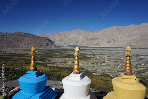 Tablou pe pânză Three colorful traditional Buddhist stupas with a beautiful mountain valley in t