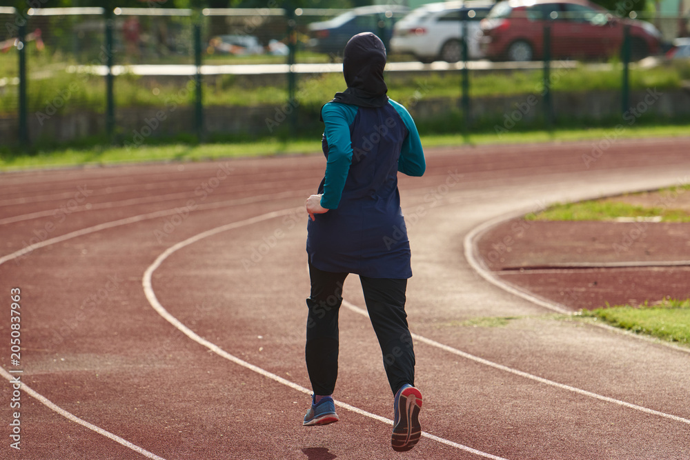 Obraz premium Woman in Hijab Running on Outdoor Track for Fitness and Training in Modest Sportswear