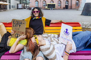 Friends holding equality signs relaxing on a rainbow bench outdoors